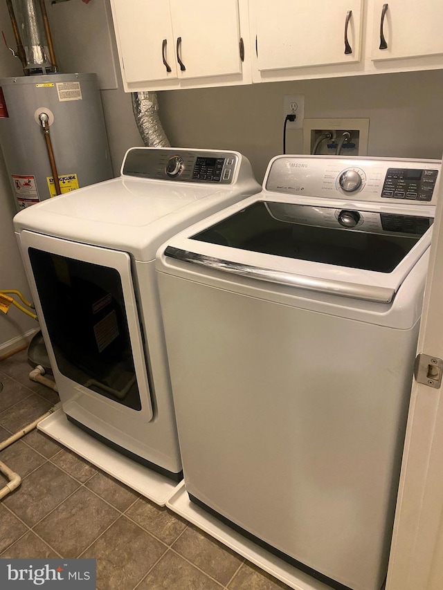 laundry room featuring cabinets, water heater, dark tile patterned floors, and washing machine and clothes dryer