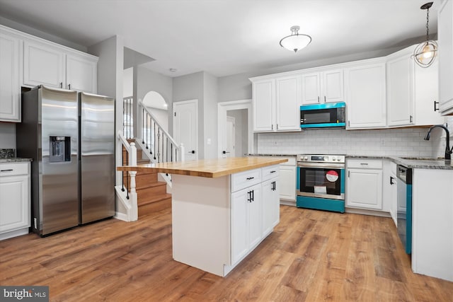 kitchen featuring white cabinetry, hanging light fixtures, stainless steel appliances, butcher block countertops, and light wood-type flooring