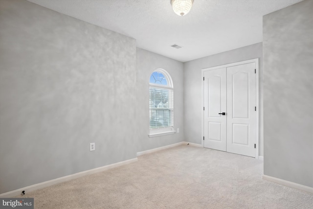 unfurnished bedroom featuring a textured ceiling, light carpet, and a closet