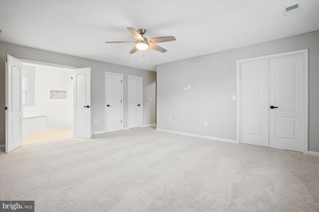 unfurnished bedroom with light colored carpet, ceiling fan, multiple closets, and ensuite bathroom