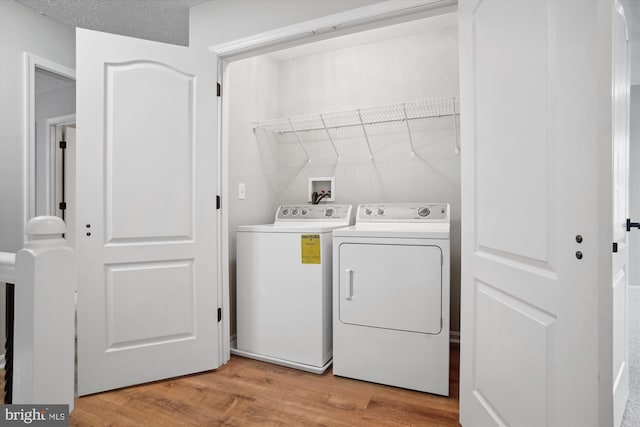 clothes washing area featuring washer and dryer, a textured ceiling, and light hardwood / wood-style flooring