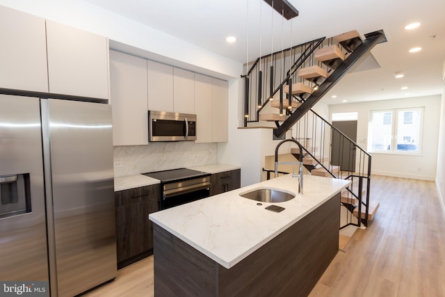 kitchen with a center island with sink, decorative light fixtures, light stone counters, white cabinetry, and stainless steel appliances