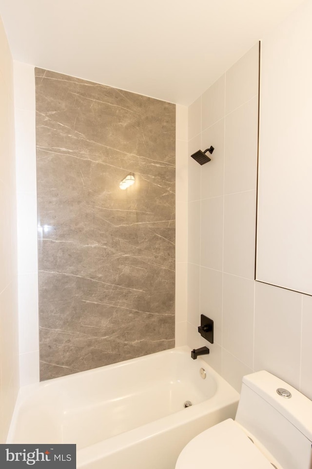 bathroom featuring tiled shower / bath, toilet, and tile walls