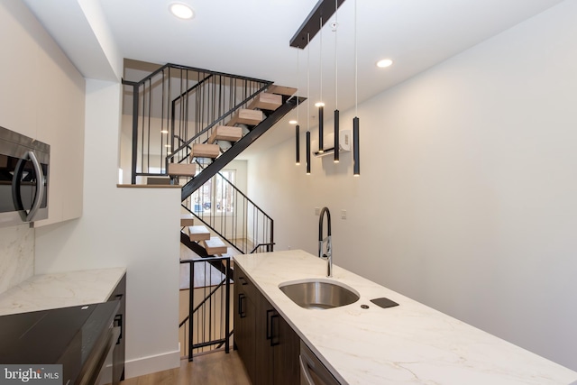 bar with light stone countertops, sink, pendant lighting, dark brown cabinets, and hardwood / wood-style flooring