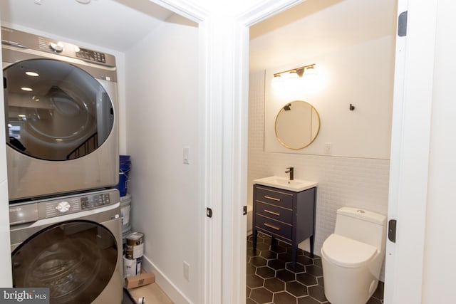 washroom with stacked washer / drying machine, sink, dark tile patterned floors, and tile walls