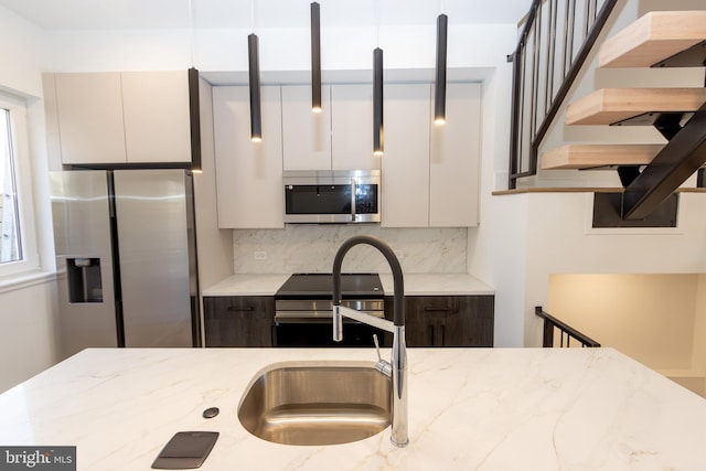 kitchen featuring backsplash, white cabinets, sink, light stone countertops, and appliances with stainless steel finishes