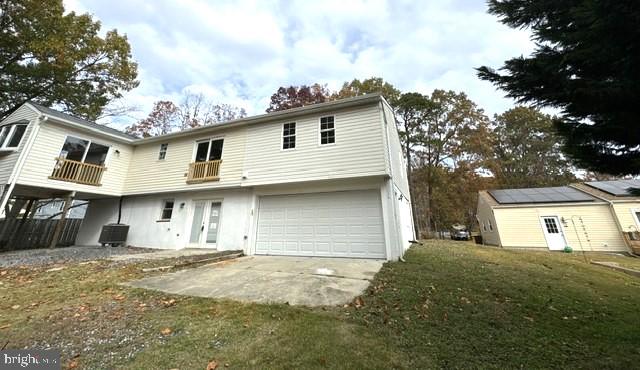 rear view of property featuring a balcony, a garage, cooling unit, and a lawn