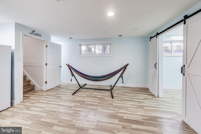 unfurnished room featuring a healthy amount of sunlight, a barn door, and light hardwood / wood-style flooring