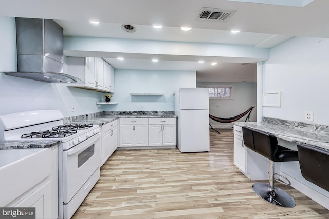 kitchen with white cabinets, light wood-type flooring, white appliances, and wall chimney range hood