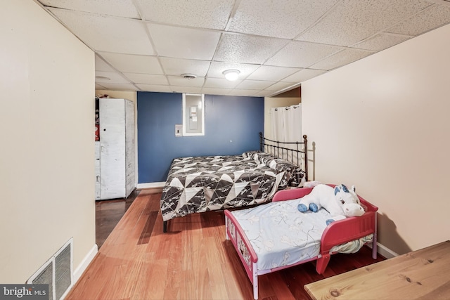 bedroom with electric panel, hardwood / wood-style floors, and a drop ceiling