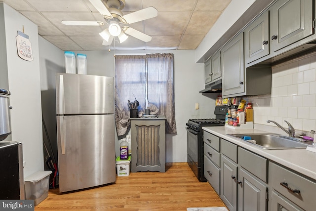 kitchen with backsplash, a drop ceiling, sink, black gas range, and stainless steel refrigerator