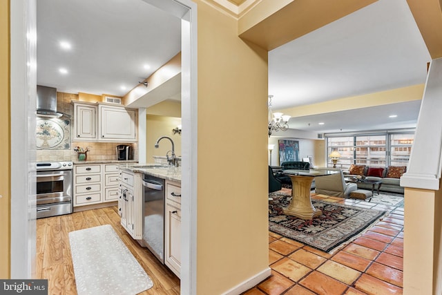 kitchen featuring sink, tasteful backsplash, appliances with stainless steel finishes, wall chimney range hood, and white cabinets