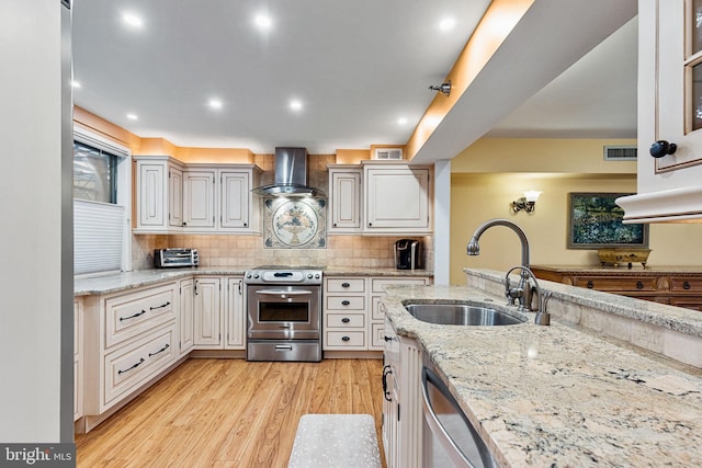 kitchen with stainless steel appliances, white cabinetry, sink, and wall chimney range hood