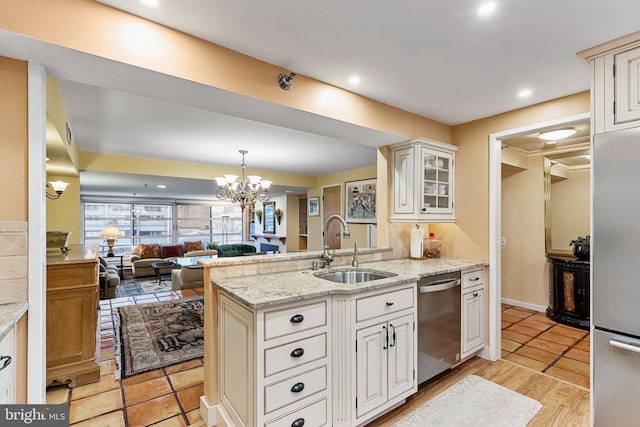 kitchen featuring sink, appliances with stainless steel finishes, light stone countertops, light hardwood / wood-style floors, and a chandelier