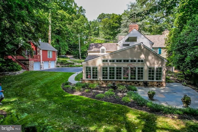 rear view of house featuring a garage, a patio area, and a lawn