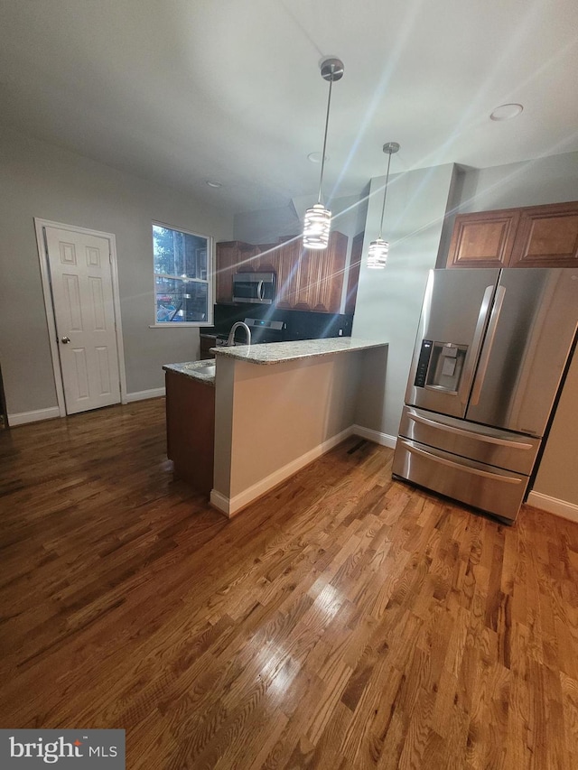 kitchen featuring stainless steel appliances, light stone counters, dark hardwood / wood-style floors, kitchen peninsula, and decorative light fixtures