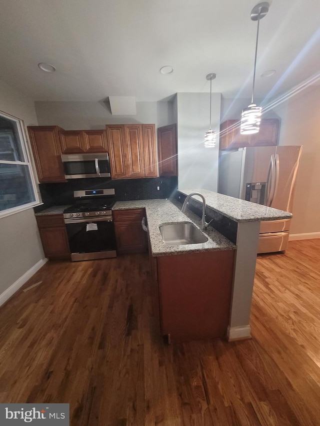 kitchen with pendant lighting, sink, dark hardwood / wood-style floors, kitchen peninsula, and stainless steel appliances