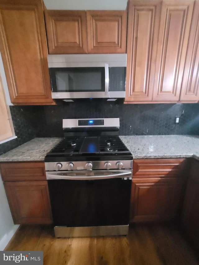 kitchen with backsplash, light stone counters, and stainless steel appliances