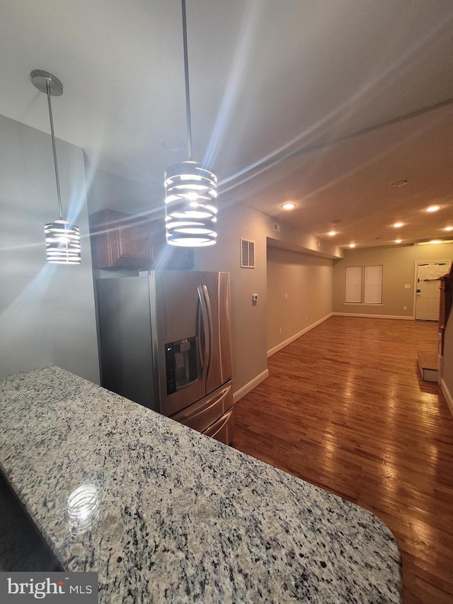 kitchen featuring decorative light fixtures, light stone countertops, stainless steel refrigerator with ice dispenser, and dark wood-type flooring