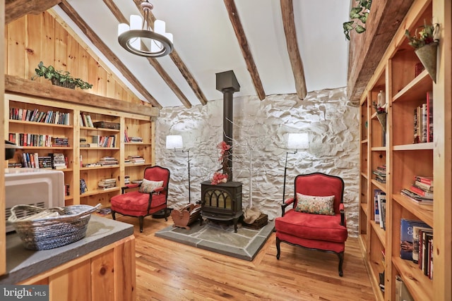 sitting room with hardwood / wood-style floors, vaulted ceiling with beams, and a wood stove