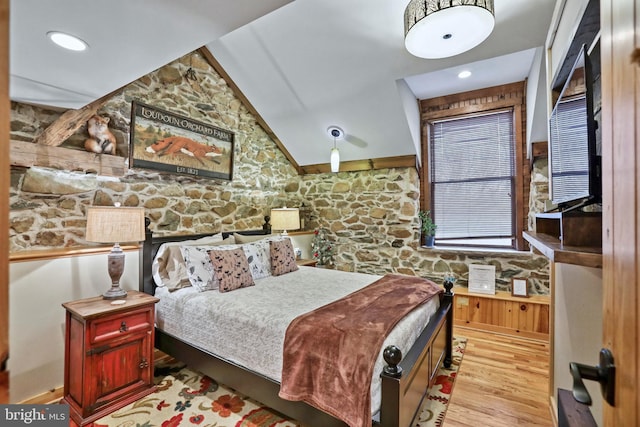 bedroom with light wood-type flooring, vaulted ceiling, and wooden walls