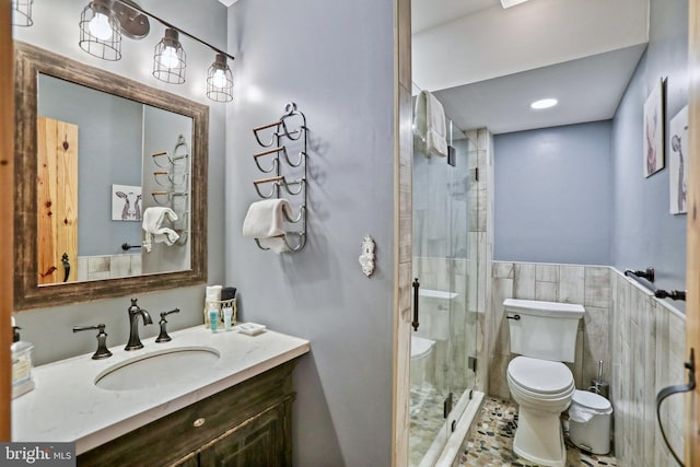 bathroom featuring vanity, toilet, a shower with shower door, and tile walls