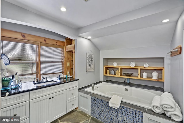 bathroom with a relaxing tiled tub, lofted ceiling, and vanity