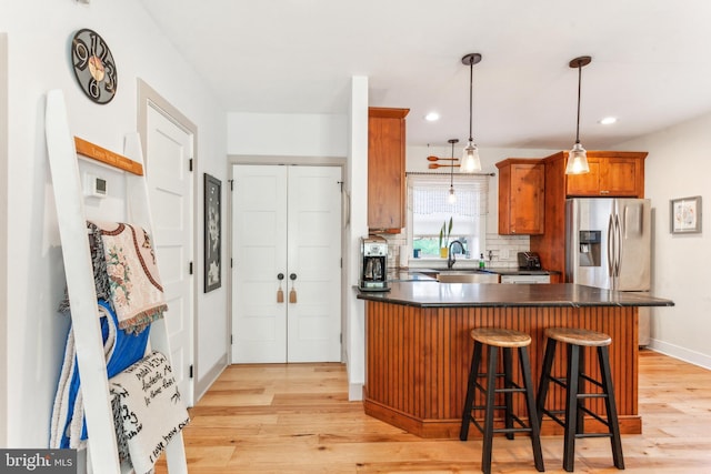 kitchen with decorative light fixtures, tasteful backsplash, sink, and light hardwood / wood-style flooring