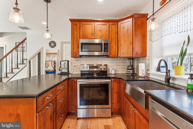 kitchen with kitchen peninsula, appliances with stainless steel finishes, light hardwood / wood-style floors, and pendant lighting