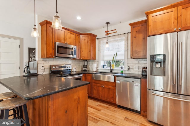 kitchen with sink, hanging light fixtures, light hardwood / wood-style flooring, a kitchen bar, and appliances with stainless steel finishes