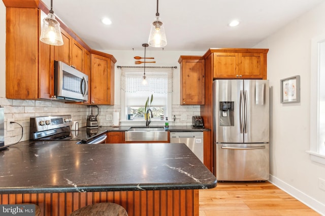 kitchen with sink, stainless steel appliances, kitchen peninsula, light hardwood / wood-style floors, and decorative light fixtures