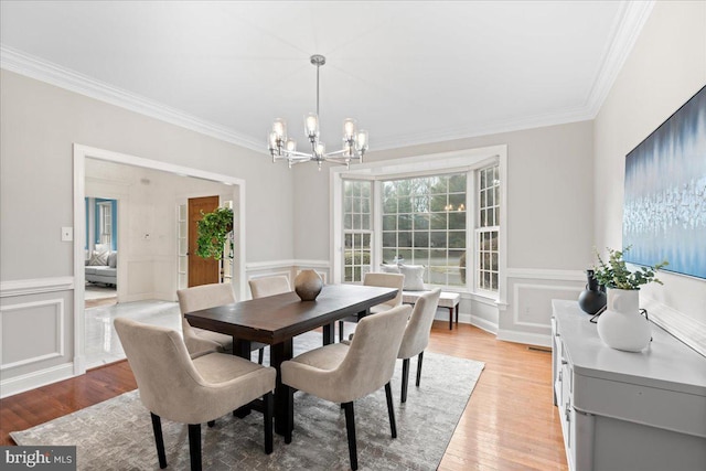 dining area with a chandelier, light wood-type flooring, and ornamental molding