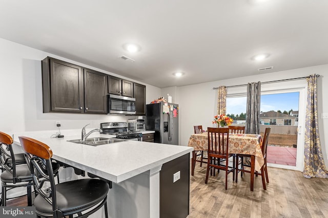 kitchen featuring a kitchen breakfast bar, sink, light wood-type flooring, appliances with stainless steel finishes, and dark brown cabinetry