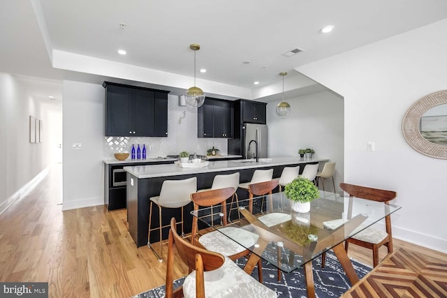 kitchen with stainless steel fridge, backsplash, decorative light fixtures, light hardwood / wood-style flooring, and a breakfast bar area