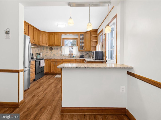 kitchen featuring hanging light fixtures, black / electric stove, light stone counters, kitchen peninsula, and stainless steel refrigerator