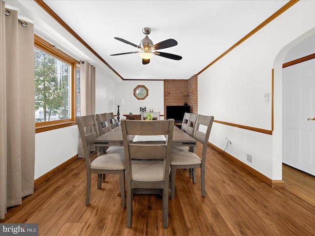 dining area with hardwood / wood-style flooring, ceiling fan, a fireplace, and crown molding