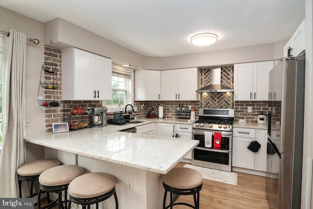 kitchen with a kitchen bar, wall chimney range hood, kitchen peninsula, and appliances with stainless steel finishes