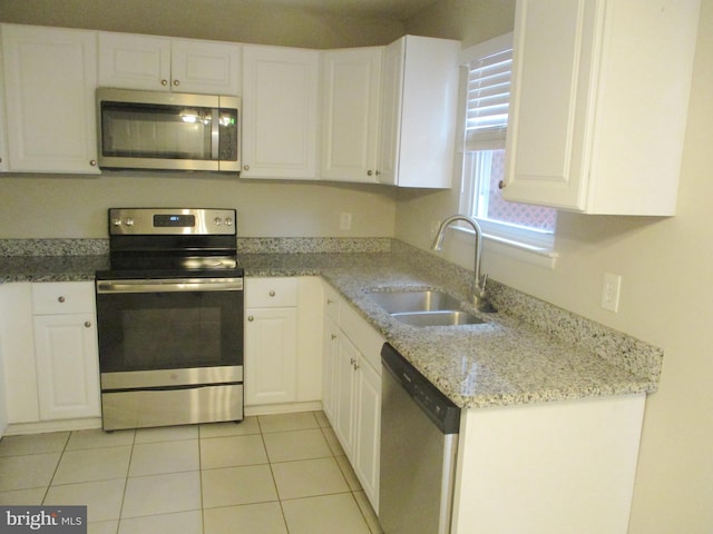 kitchen featuring appliances with stainless steel finishes, light stone counters, sink, light tile patterned floors, and white cabinetry