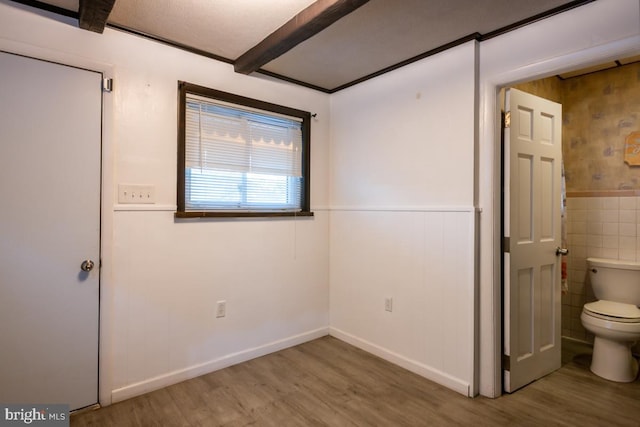 unfurnished room with beam ceiling, wood-type flooring, and tile walls