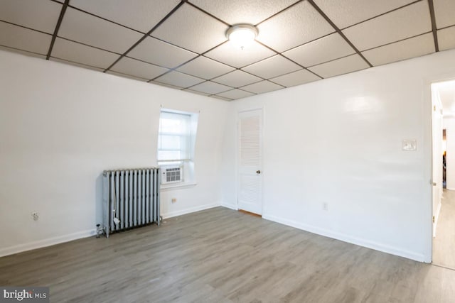 empty room featuring hardwood / wood-style flooring, a paneled ceiling, and radiator heating unit