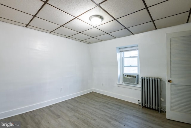 spare room featuring radiator heating unit, a paneled ceiling, hardwood / wood-style flooring, and cooling unit