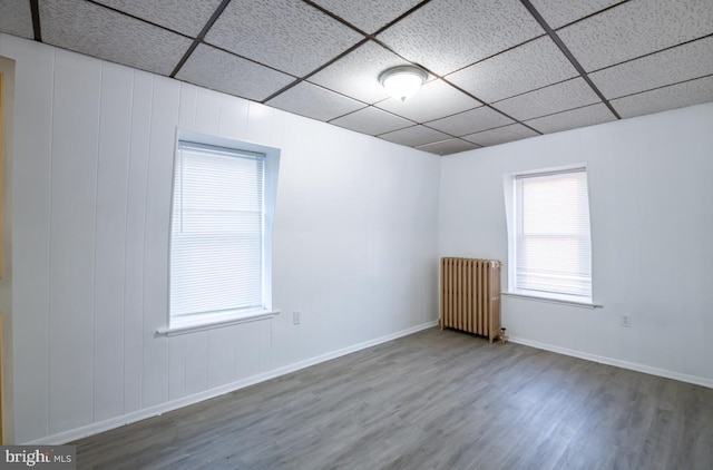 empty room with radiator heating unit, a drop ceiling, and wood-type flooring