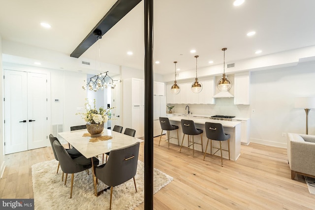 dining space featuring an inviting chandelier, sink, and light hardwood / wood-style flooring