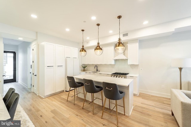 kitchen with white fridge, white cabinets, a kitchen breakfast bar, decorative light fixtures, and light hardwood / wood-style floors