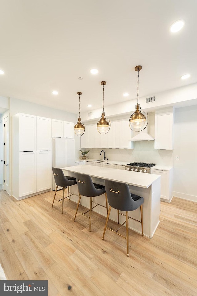 bar featuring white cabinets, light hardwood / wood-style floors, decorative light fixtures, white fridge, and stainless steel gas cooktop