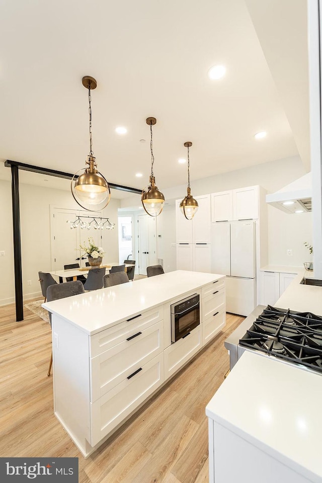 kitchen with white refrigerator, light hardwood / wood-style floors, decorative light fixtures, a kitchen island, and white cabinetry