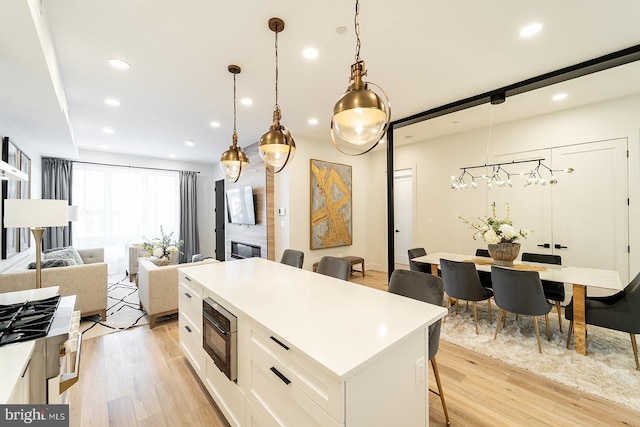 kitchen with a kitchen breakfast bar, a kitchen island, decorative light fixtures, light hardwood / wood-style flooring, and white cabinetry