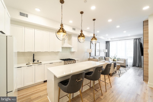 kitchen with a center island, hanging light fixtures, light hardwood / wood-style flooring, white refrigerator, and white cabinets