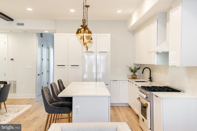 kitchen featuring high end range, light hardwood / wood-style floors, stainless steel refrigerator, and sink