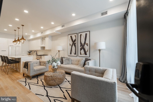 living room with a chandelier, sink, and light hardwood / wood-style flooring